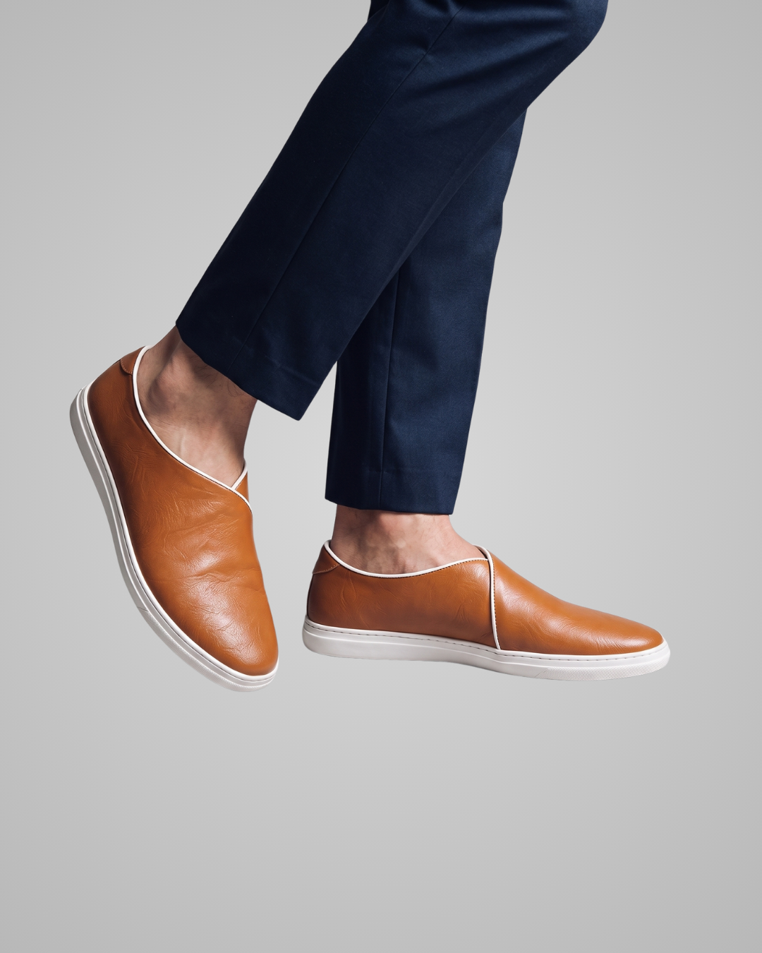 Brown leather shoes worn with navy pants on a gray background