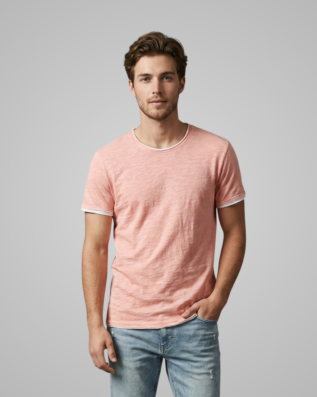 Man wearing a pink t-shirt and light blue jeans against a gray background