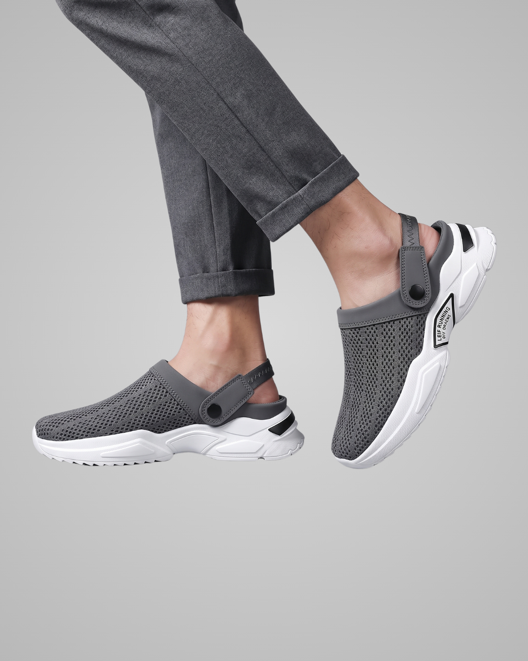 Person wearing gray mesh clogs with white soles on a light gray background