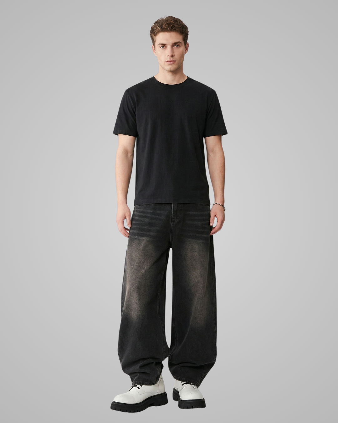 Man wearing a black t-shirt and dark jeans on a gray background