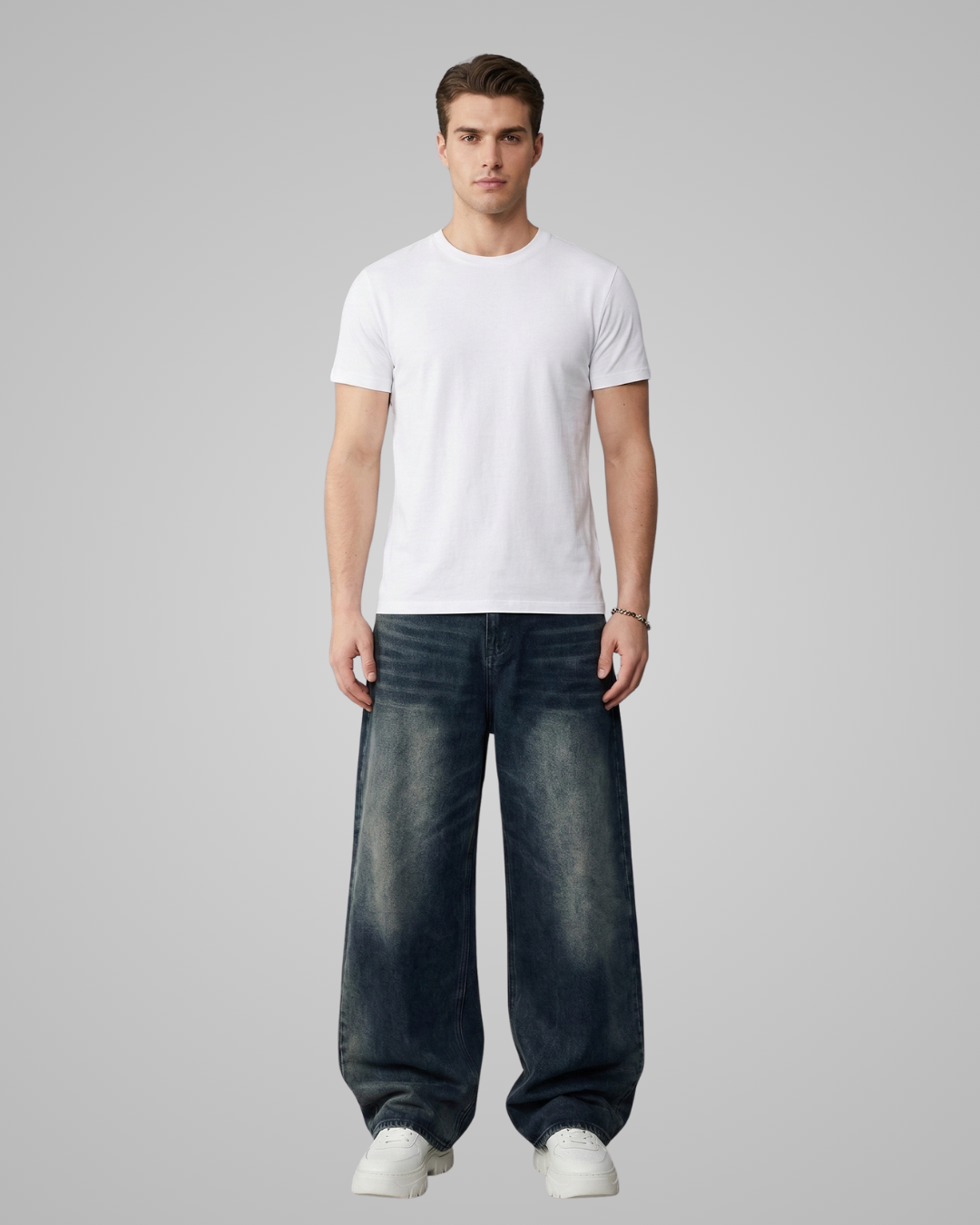 Man wearing a plain white t-shirt and dark jeans on a gray background