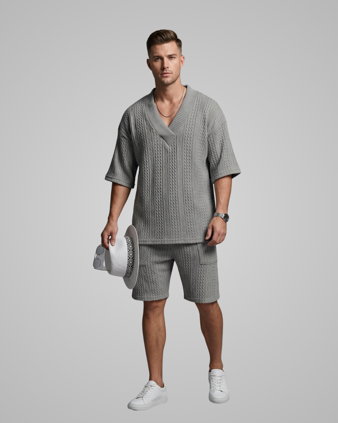 Man wearing a gray knit outfit holding a white hat against a plain background
