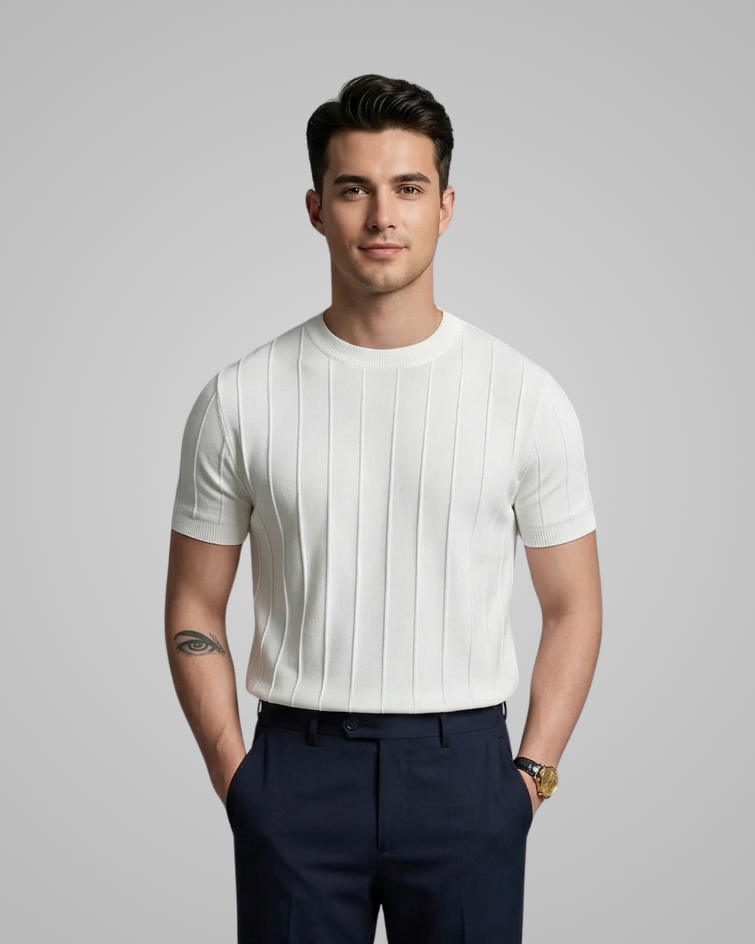 Man wearing a white ribbed knit t-shirt and dark pants on a gray background