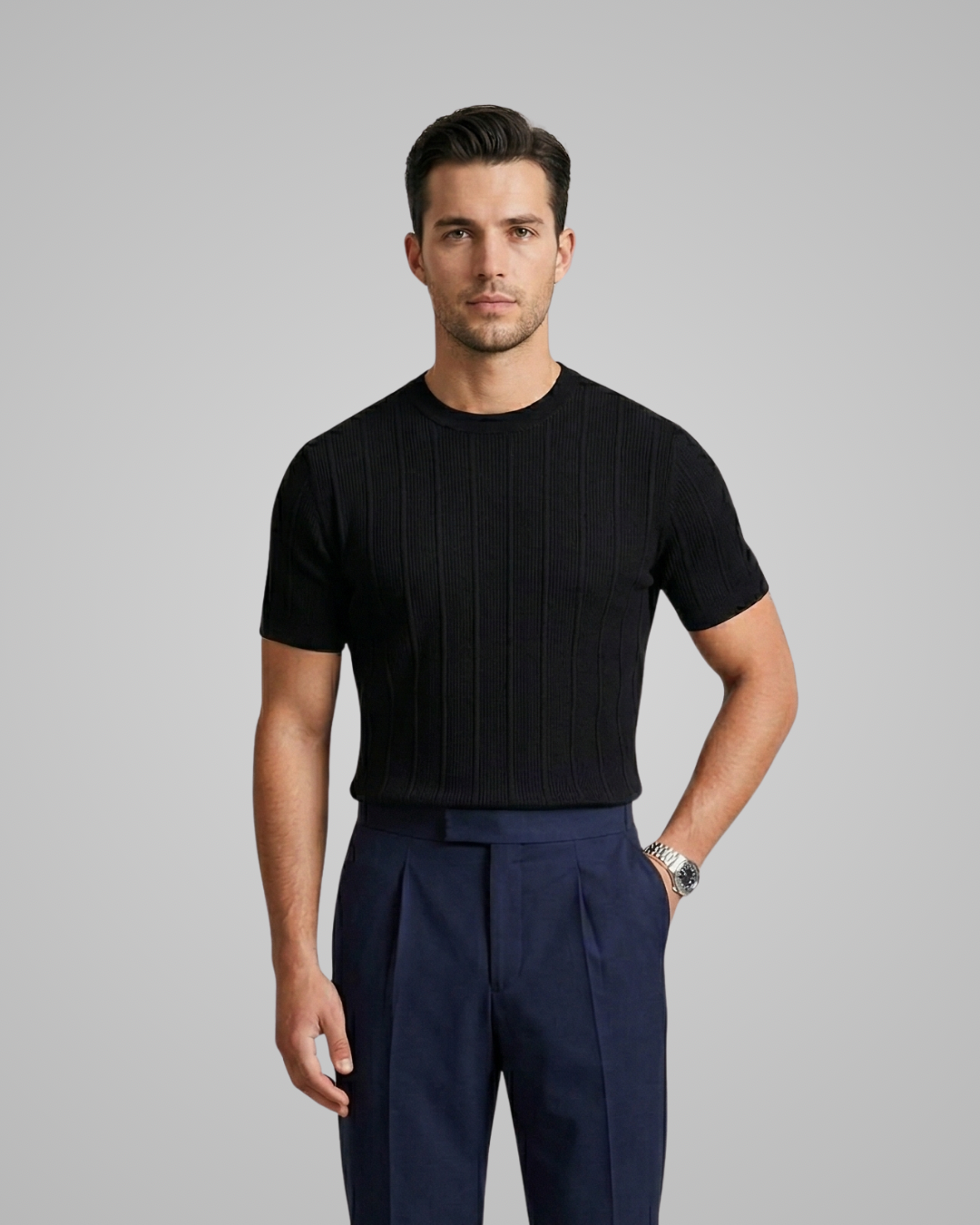 Man wearing a black ribbed sweater and navy pleated pants on a gray background