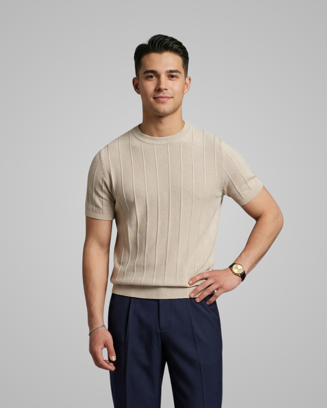 Man wearing a beige ribbed sweater and navy pants against a gray background