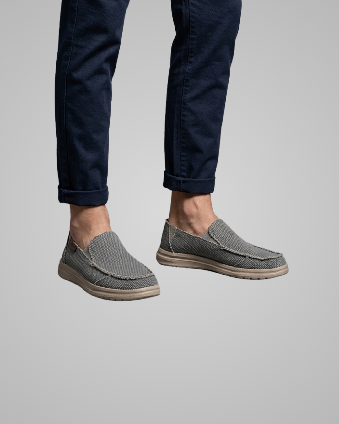 Gray slip-on shoes worn with navy pants on a gray background