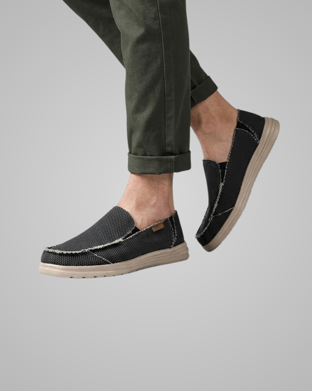 Person wearing black casual shoes with beige soles on a gray background