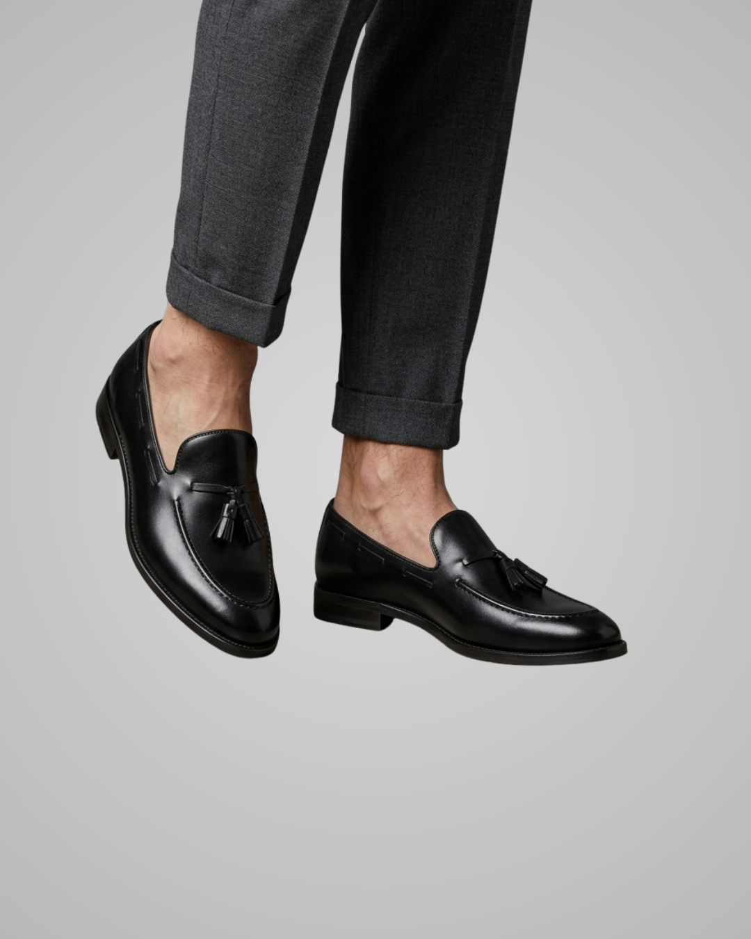 Black loafers worn with gray pants on a light gray background