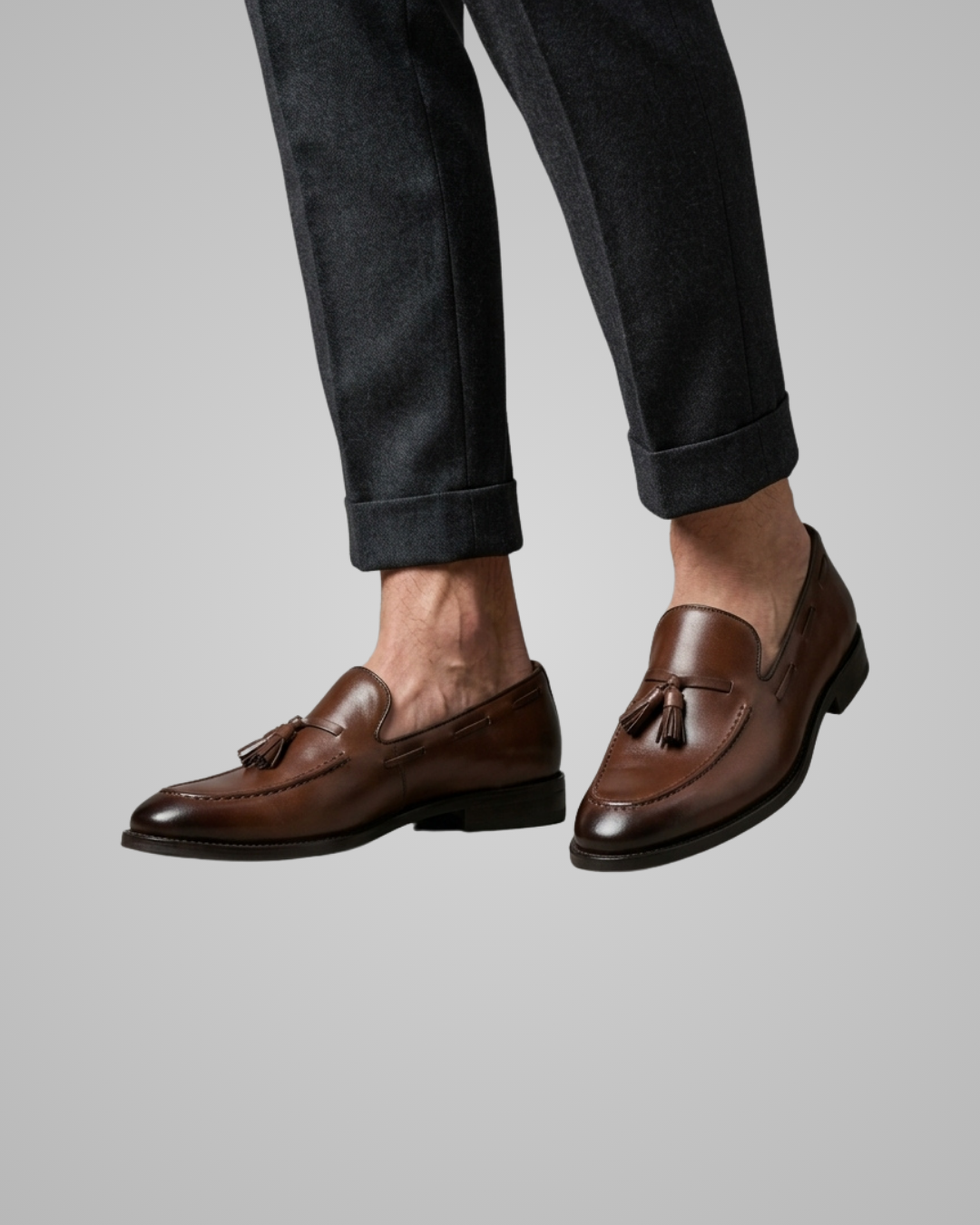 Brown loafers worn with dark jeans on a plain background