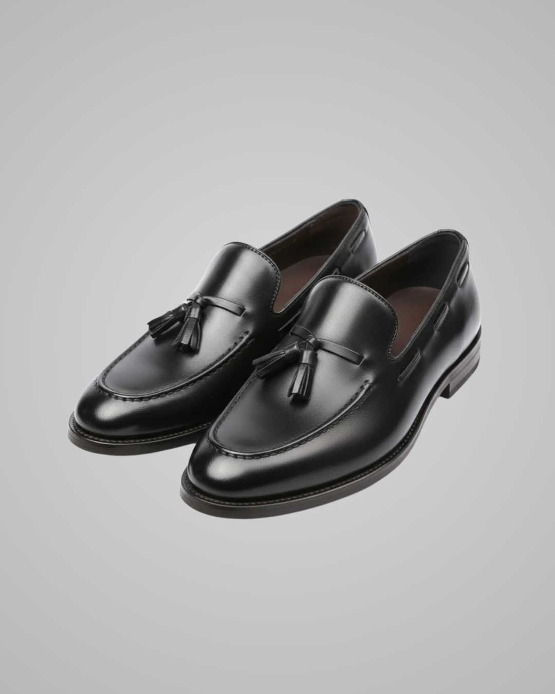 Pair of black loafers with tassels on a gray background