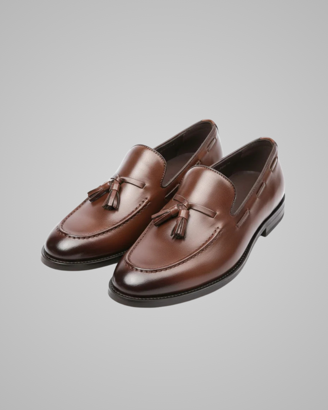 Pair of brown loafers with tassels on a gray background
