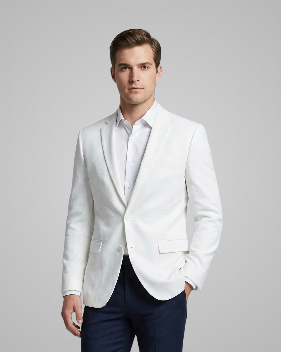 Man wearing a white blazer over a light shirt with navy pants on a gray background
