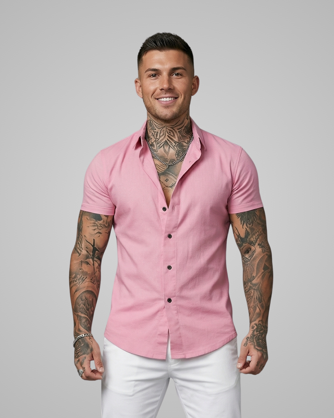Man wearing a pink shirt and white pants with tattoos on arms against a gray background
