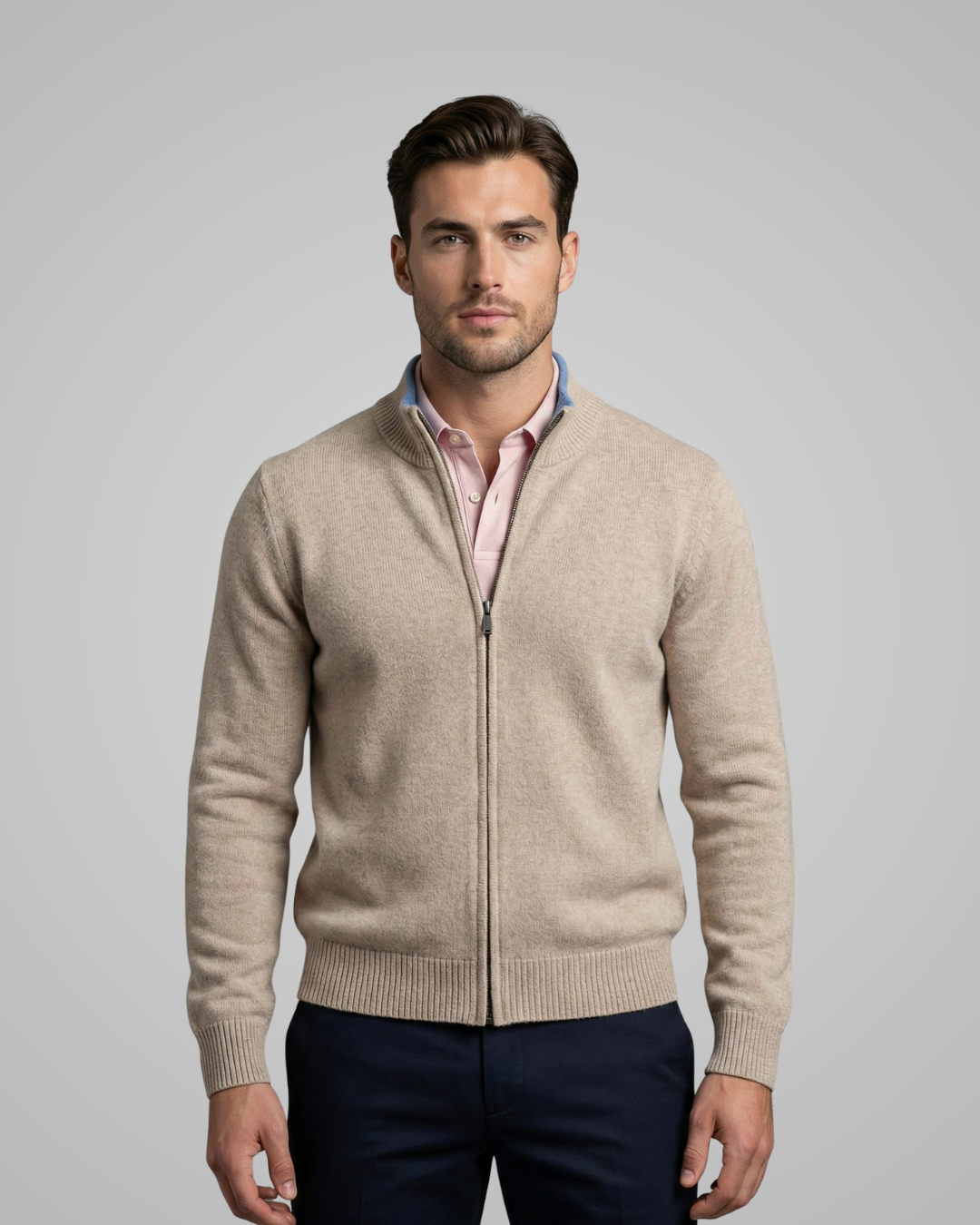 Man wearing a beige zip-up sweater over a pink shirt on a gray background