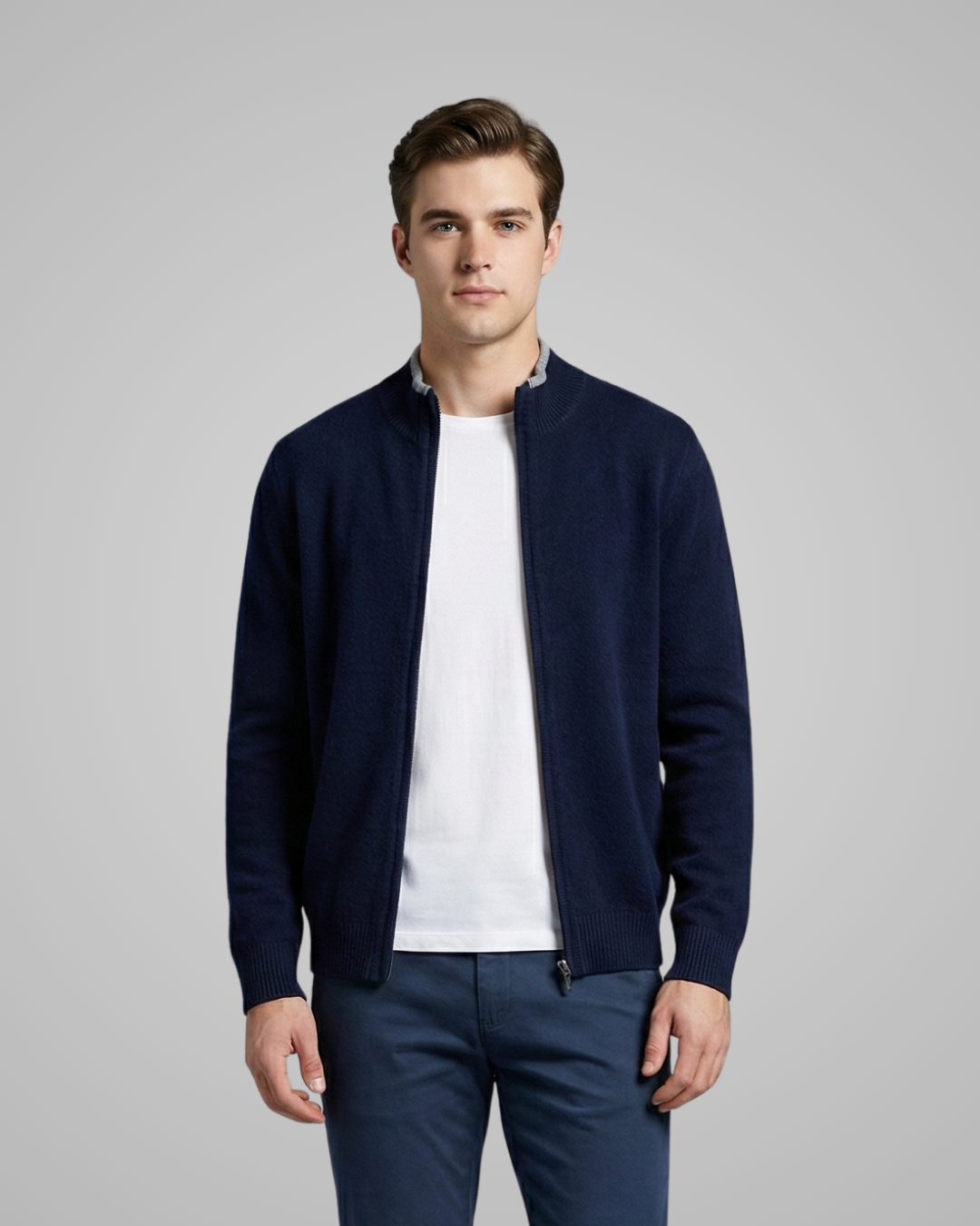 Man wearing a navy blue cardigan over a white shirt and blue pants on a gray background