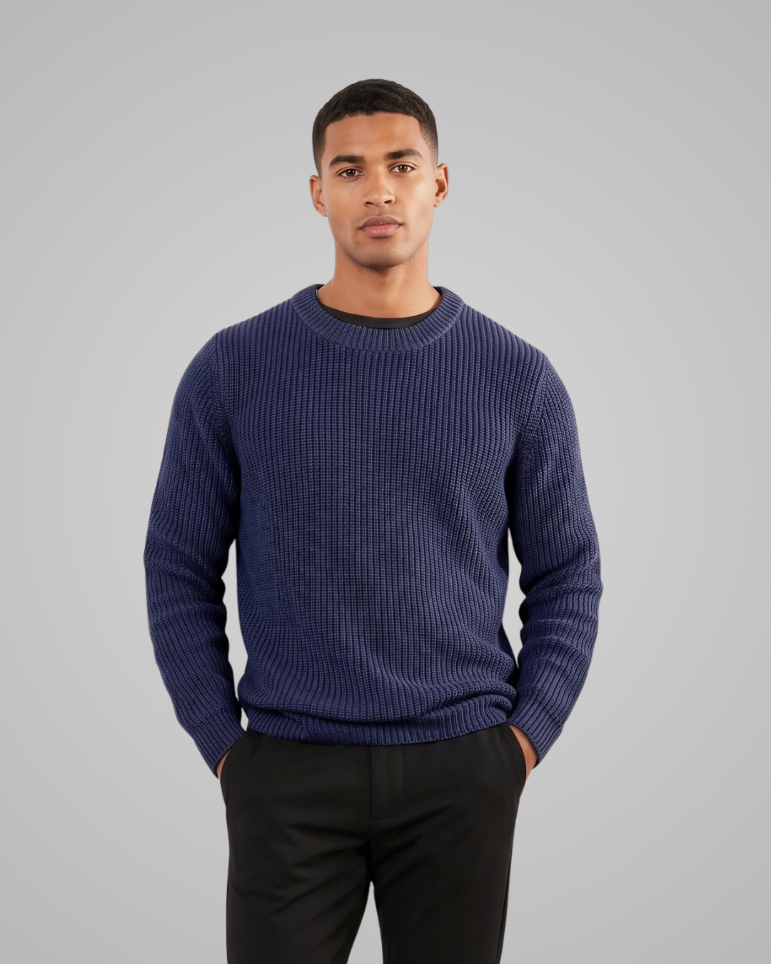 Man wearing a blue sweater and black pants against a gray background
