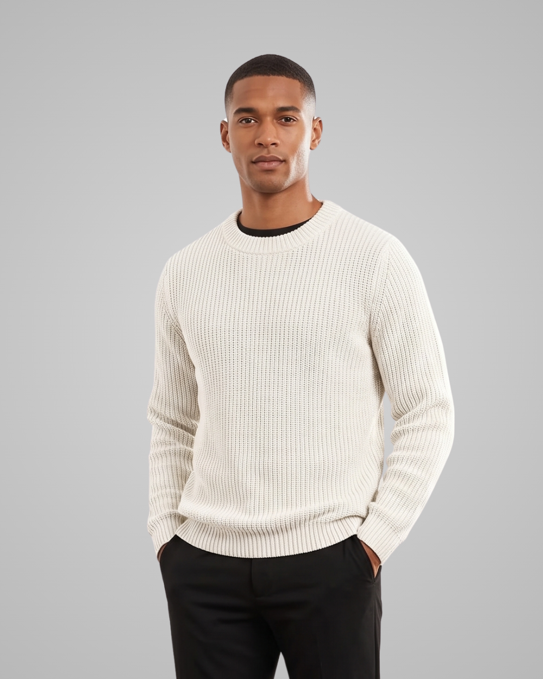 Man wearing a cream sweater and black pants against a gray background