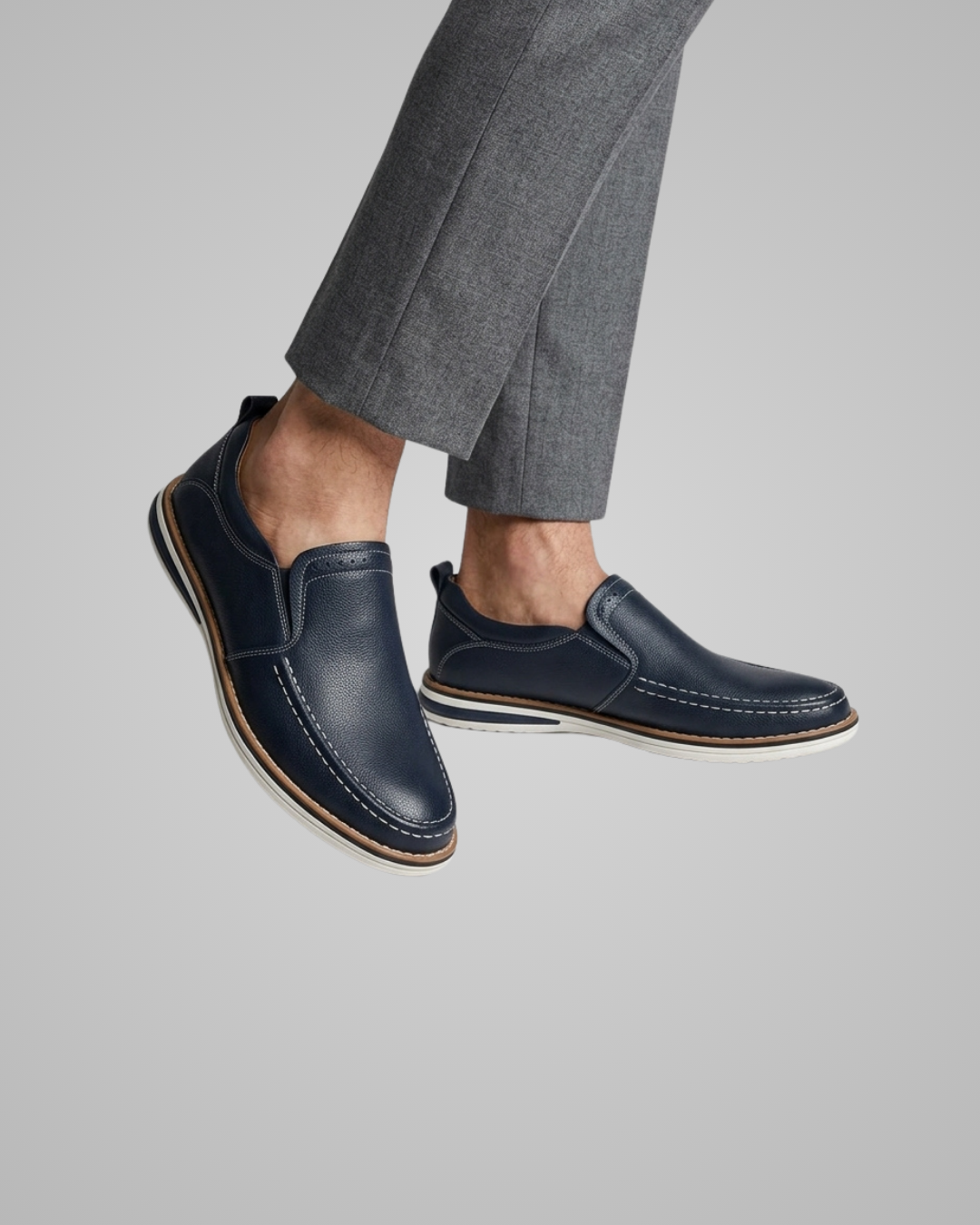 Navy loafers worn with gray trousers on a neutral background