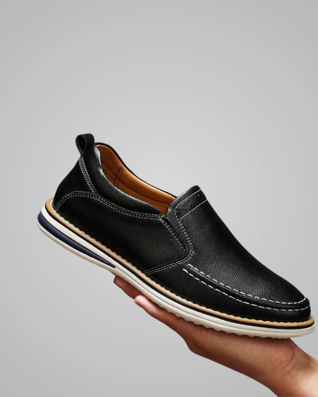Black slip-on shoe held in a hand against a gray background