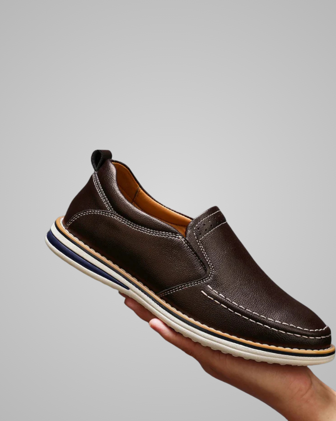 Brown leather slip-on shoe held by a hand against a gray background