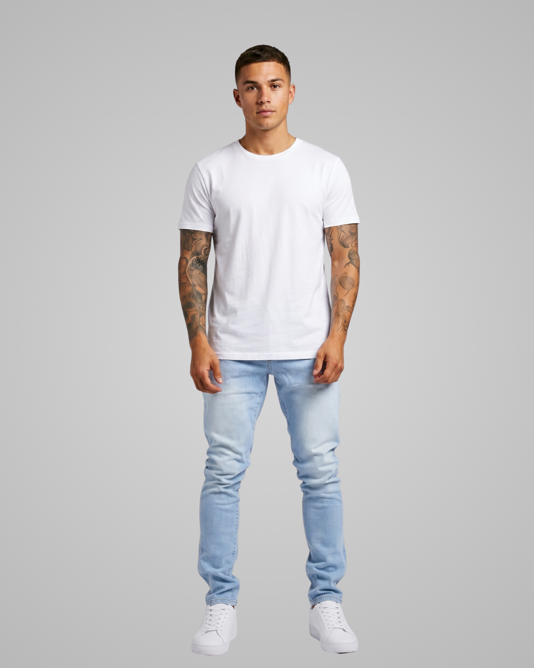 Man wearing a plain white t-shirt and light blue jeans on a gray background