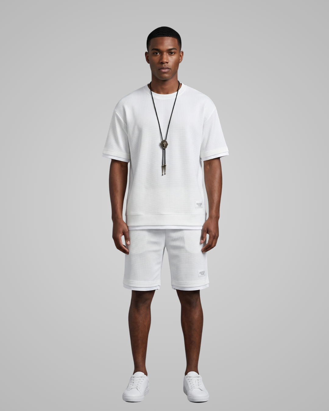 Man wearing a white t-shirt and shorts with a necklace on a gray background