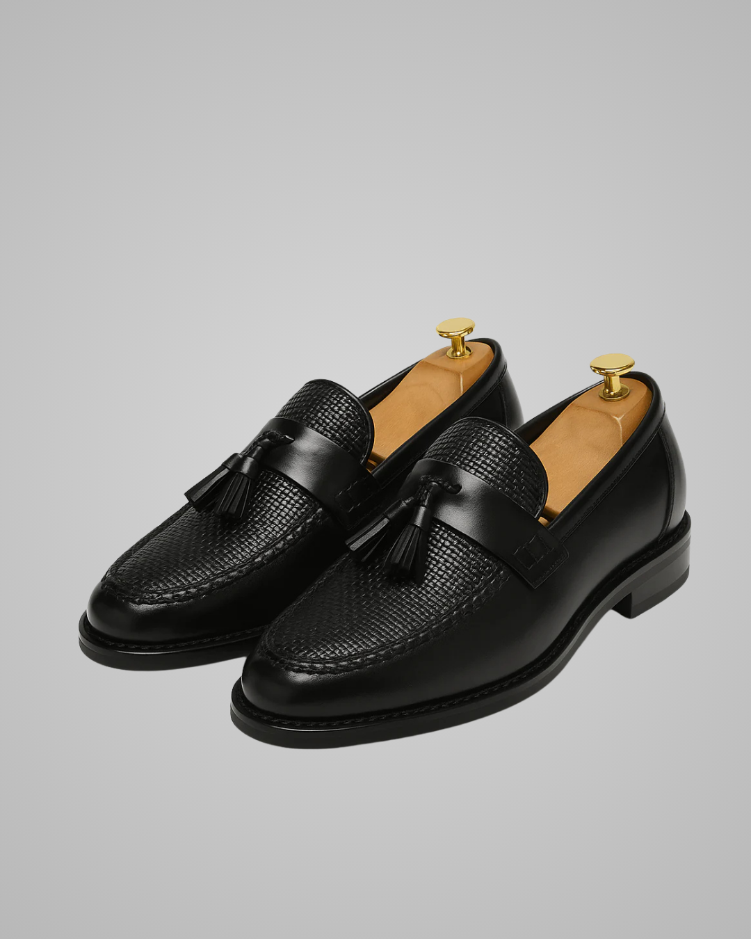 Pair of black leather loafers with tassels on a gray background