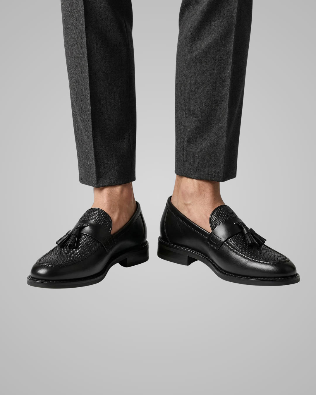 Black loafers worn with black pants on a gray background