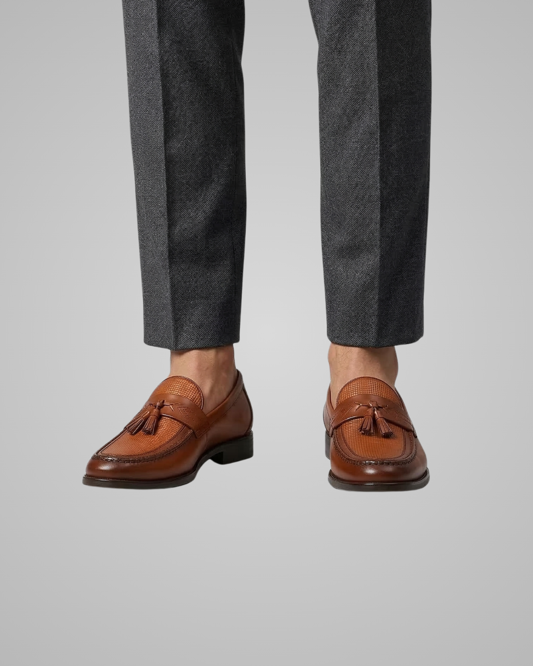 Brown loafers worn with gray trousers on a light gray background