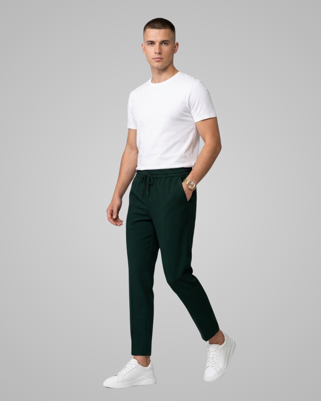 Man wearing a white t-shirt and dark green pants on a gray background
