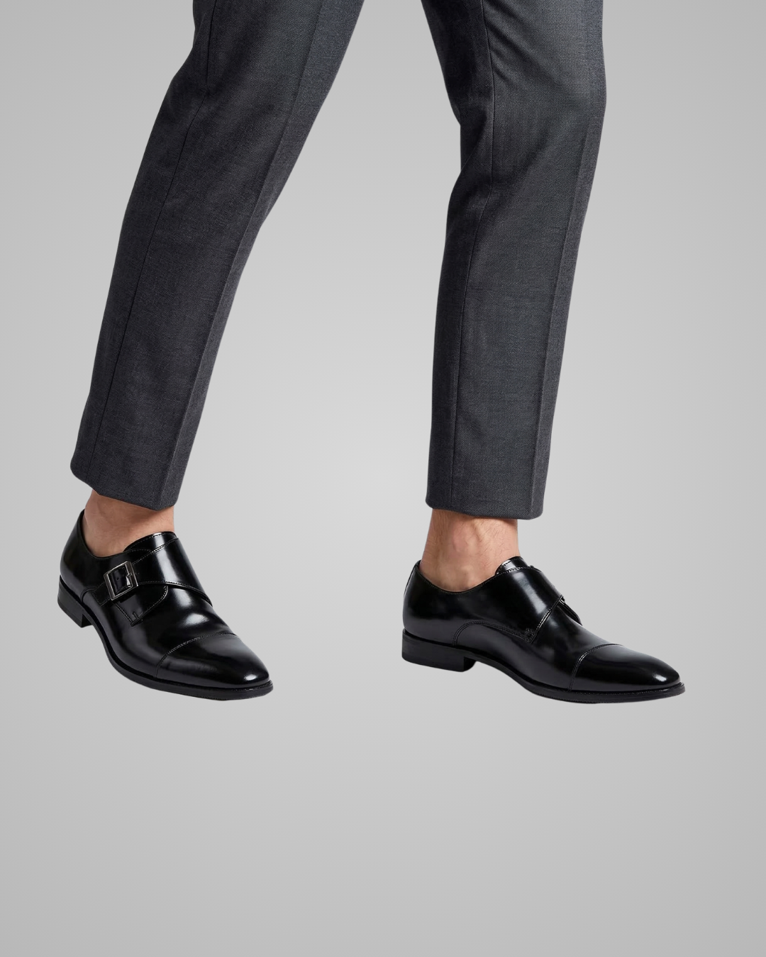 Black dress shoes worn with gray pants on a light gray background