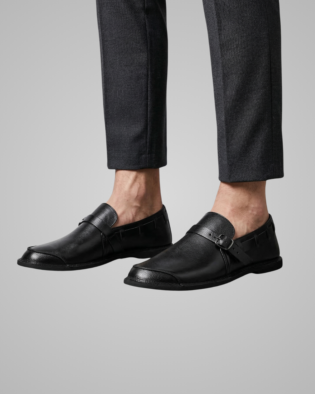 Black loafers worn with dark trousers on a gray background