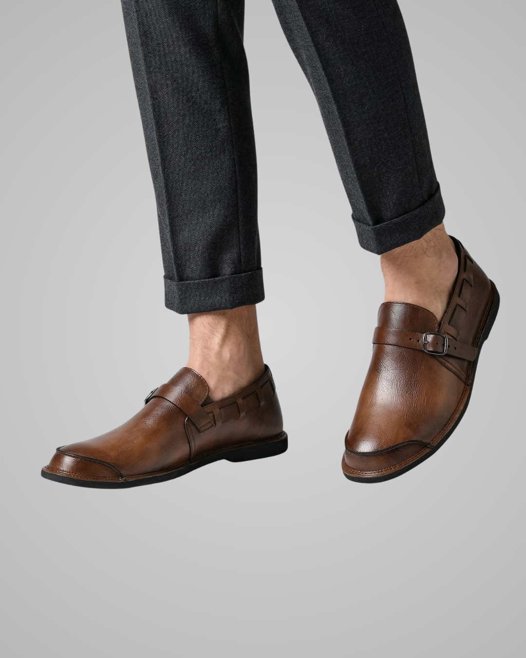 Brown dress shoes worn with dark jeans on a light gray background