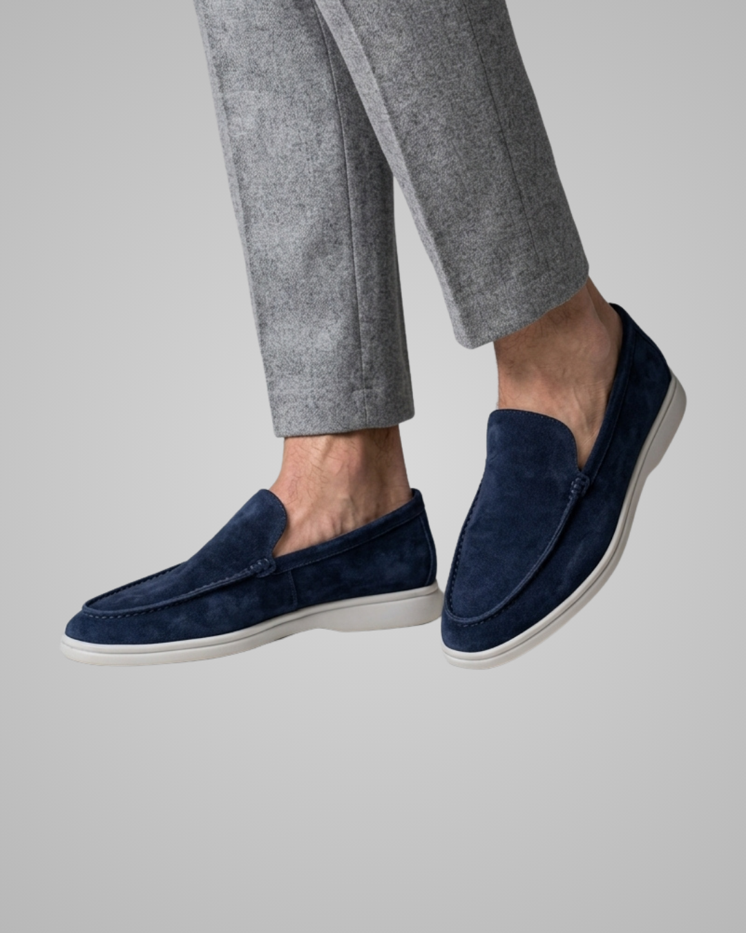 Navy loafers worn with gray pants on a neutral background