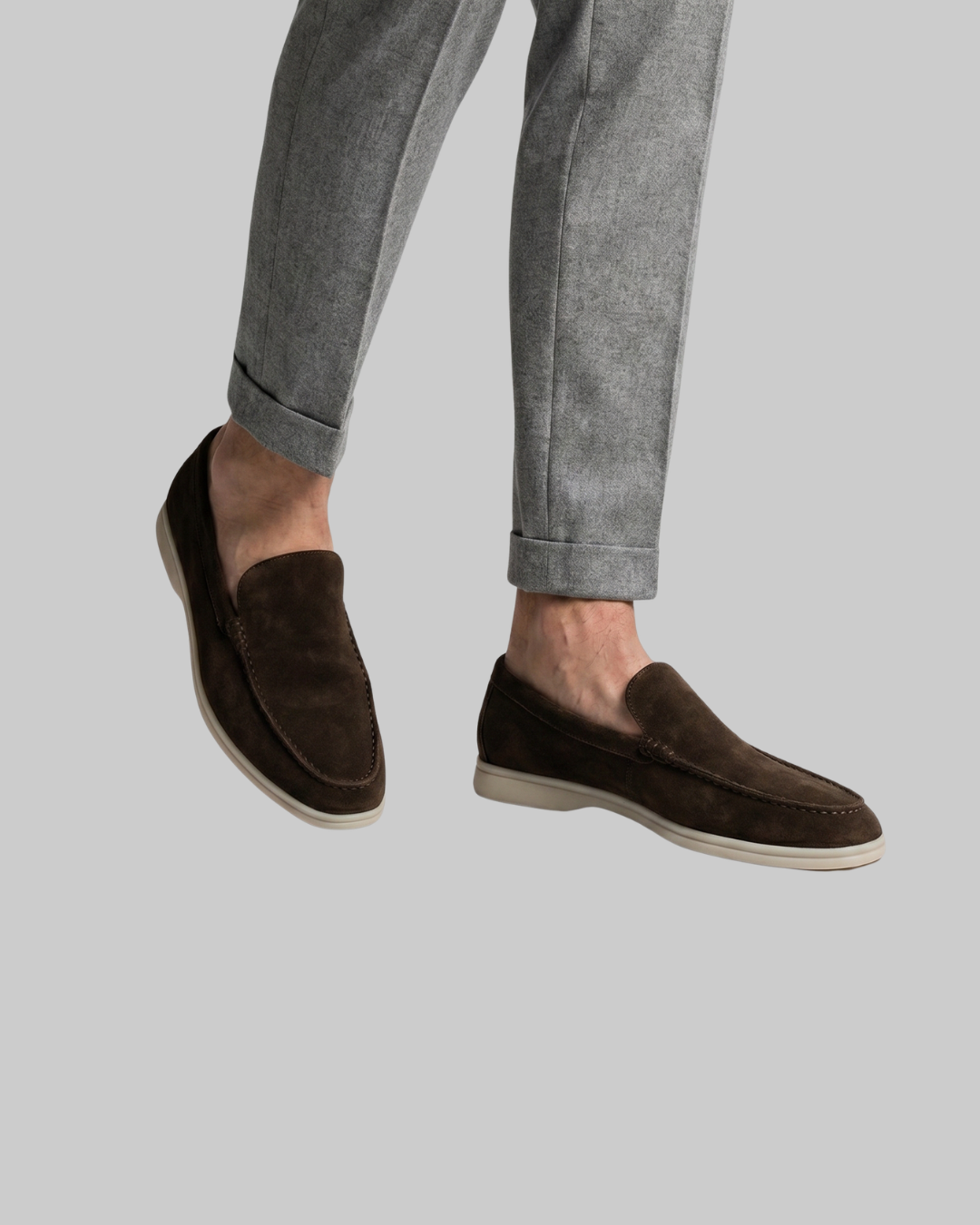 Brown loafers worn with gray pants on a light gray background