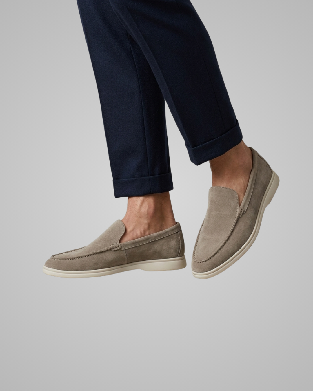 Beige loafers worn with navy pants on a light gray background