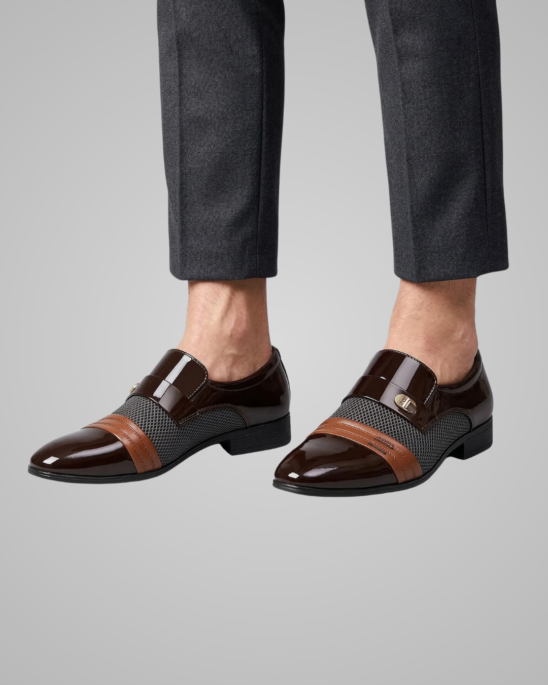 Brown dress shoes with black and brown patterned accents worn with gray pants on a light gray background