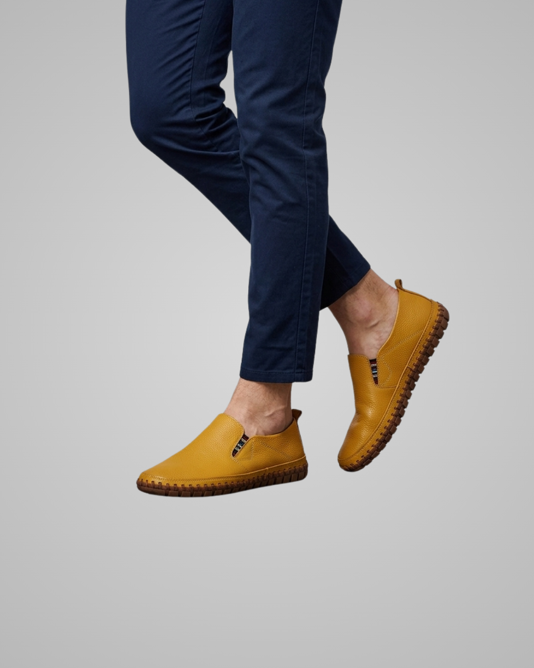 A person wearing navy blue pants and mustard yellow slip-on shoes with a textured sole, shown against a plain light gray background.