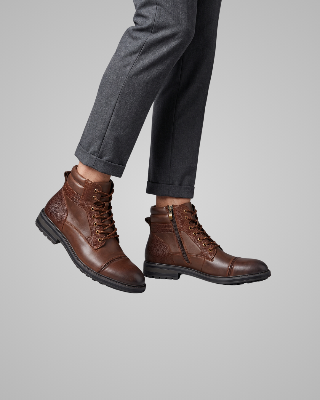 A pair of men's brown leather lace-up ankle boots with a side zipper, shown on a model wearing dark gray trousers against a solid gray background.