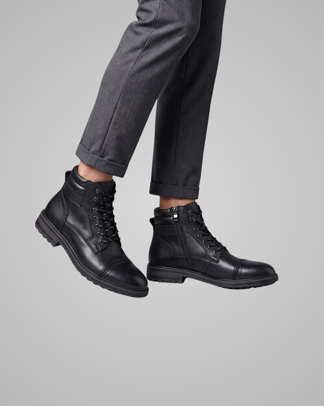 Black leather lace-up ankle boots with side zippers, shown on a model wearing dark gray trousers against a solid gray background.