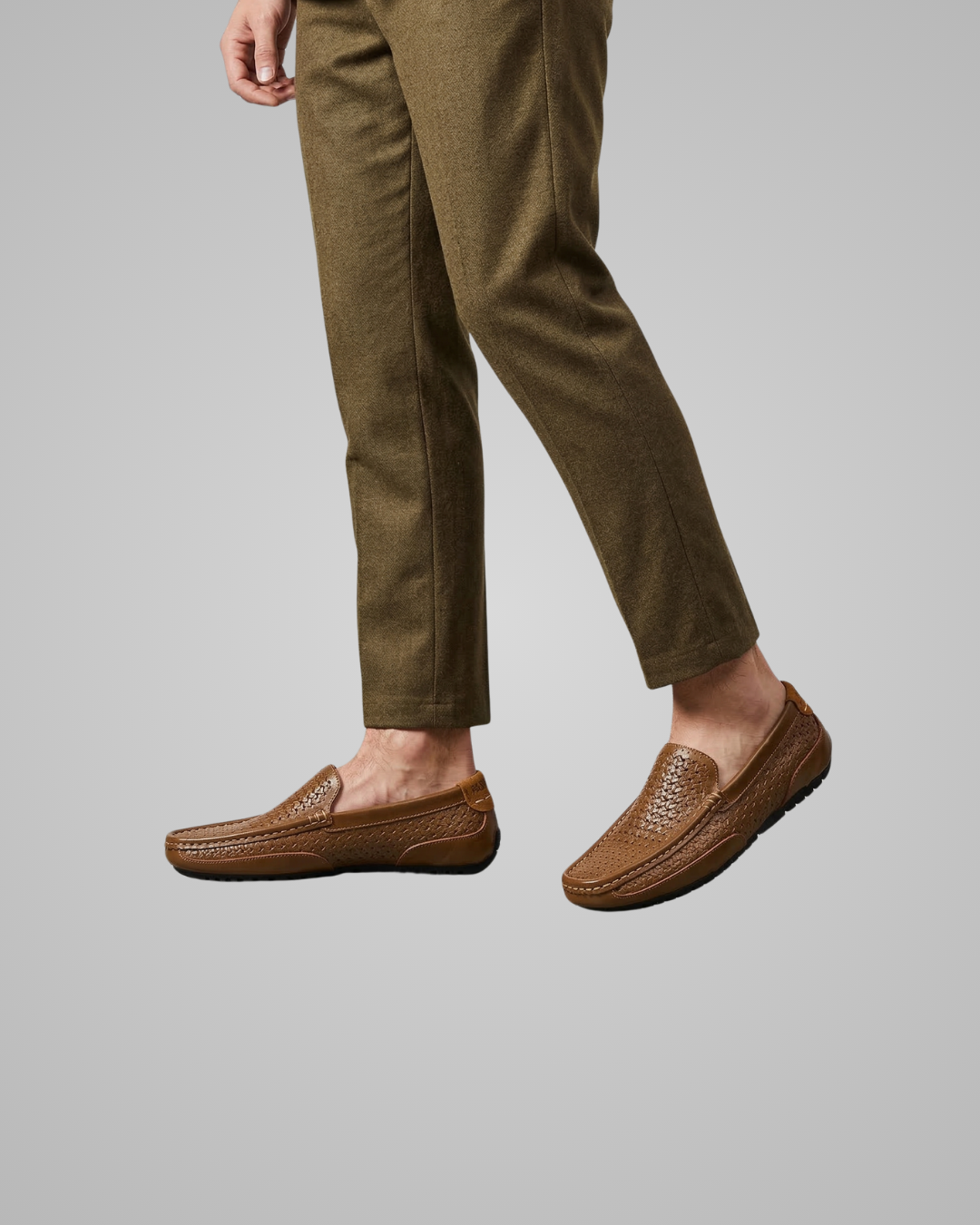 Brown loafers worn with green pants on a gray background