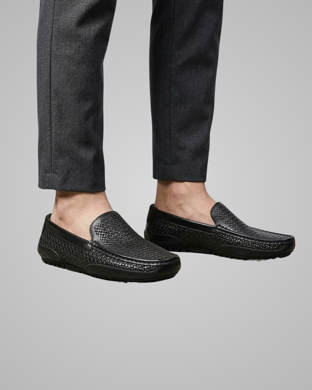 Black loafers worn with dark pants on a gray background