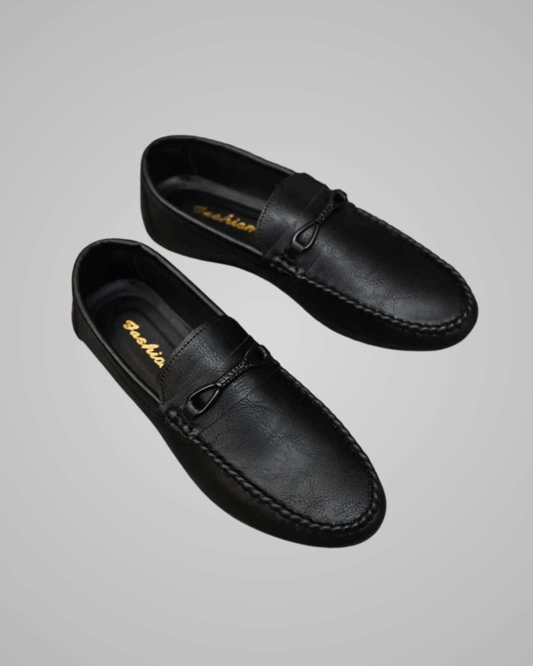 A pair of black leather penny loafers with a small leather loop detail on the vamp, displayed on a neutral gray background. The brand name 'Bashirah' is printed in gold on the insole.