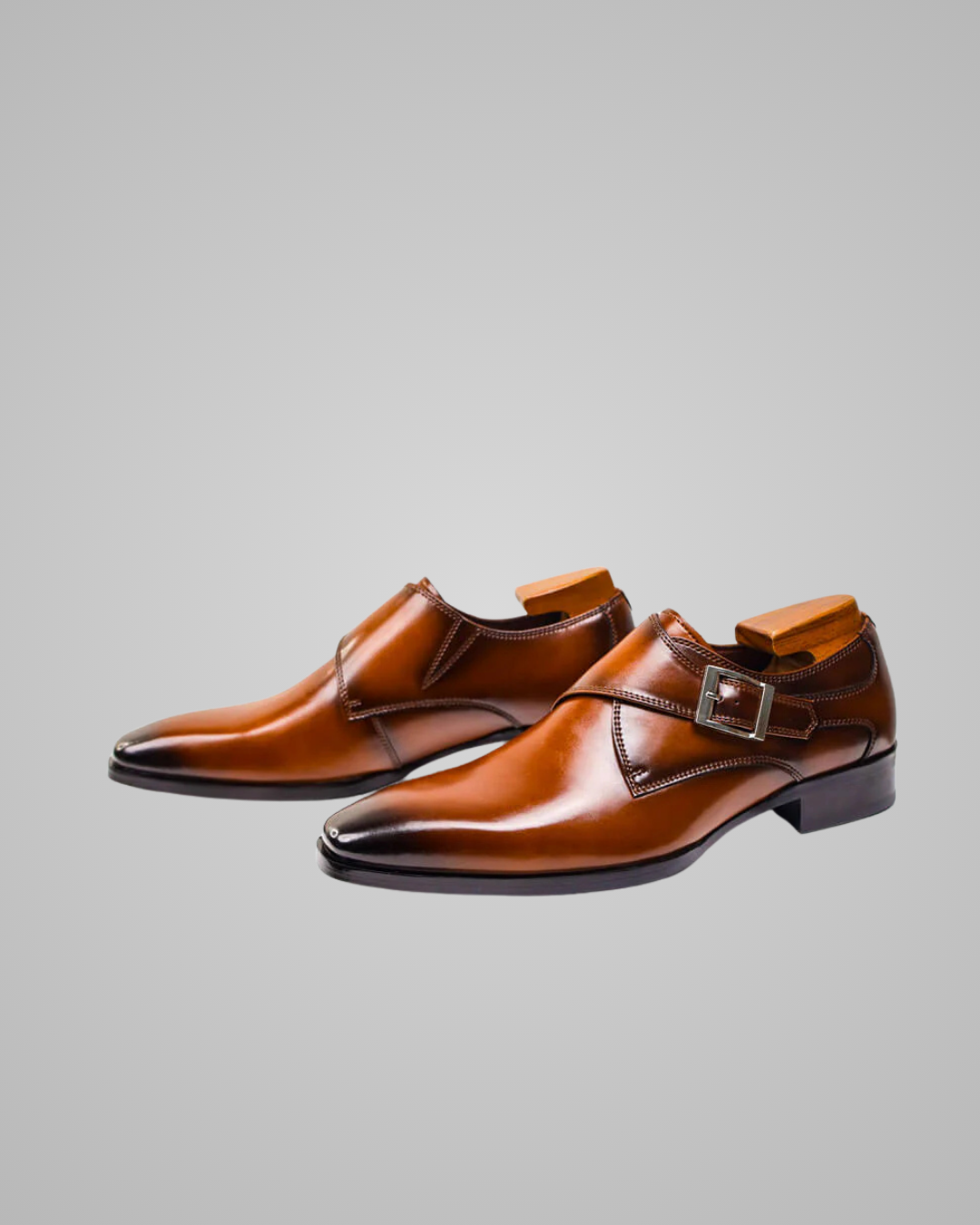 Pair of brown leather dress shoes with a buckle on a gray background