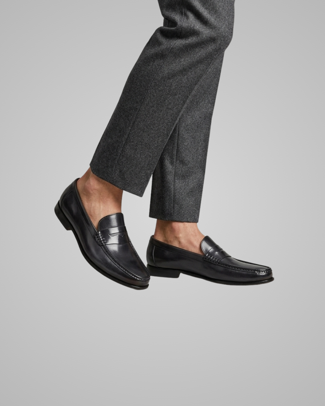 Black loafers worn with gray pants on a light gray background