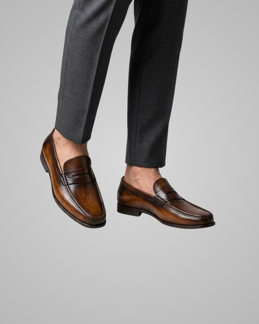 Brown loafers worn with gray pants on a light gray background
