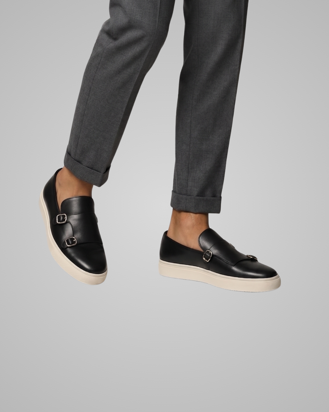 Black leather shoes worn with gray pants on a gray background