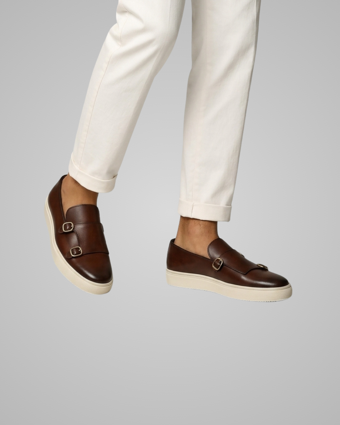 Brown loafers worn with white pants on a gray background