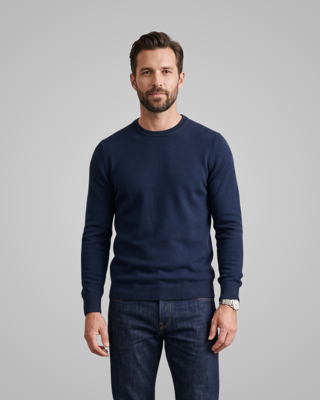 Man wearing a navy sweater and dark jeans on a gray background