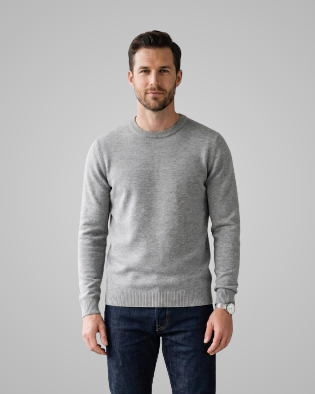 Man wearing a gray sweater and dark jeans against a plain background